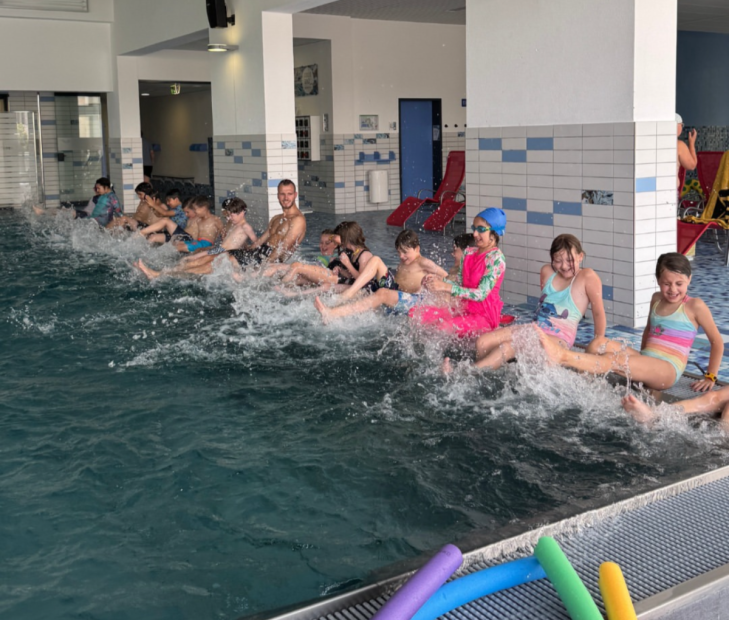 Bewegungskoordinator Marius Hamel zeigt den Kindern eine Übung zur Wassergewöhnung: Mit den Füßen ins Becken strampeln, Spritzwasser erleben und spielerisch Wasserwiderstand, Strömungen und das Element Wasser kennenlerne.    Bild: Sportkreis Waldeck-Frankenberg